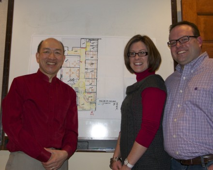 Three people standing in front of a wall with plans on it.