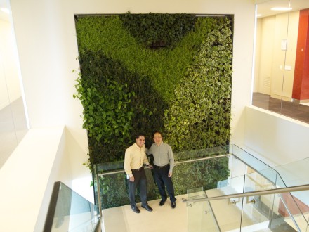 Two men standing in front of a green wall.